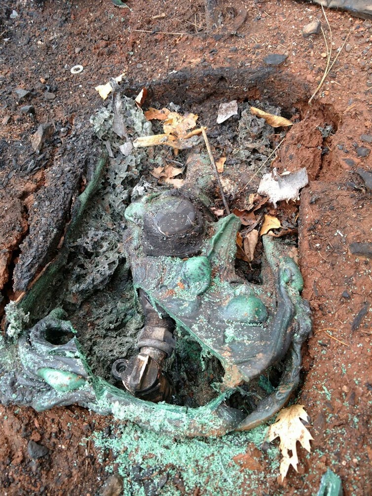 A photo shows water pipes and a meter beneath a melted plastic cover, damaged by a fire.